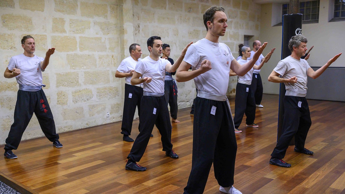 Un groupe de pratiquants tient la position du cavalier, bras levés, axe et appuis alignés.